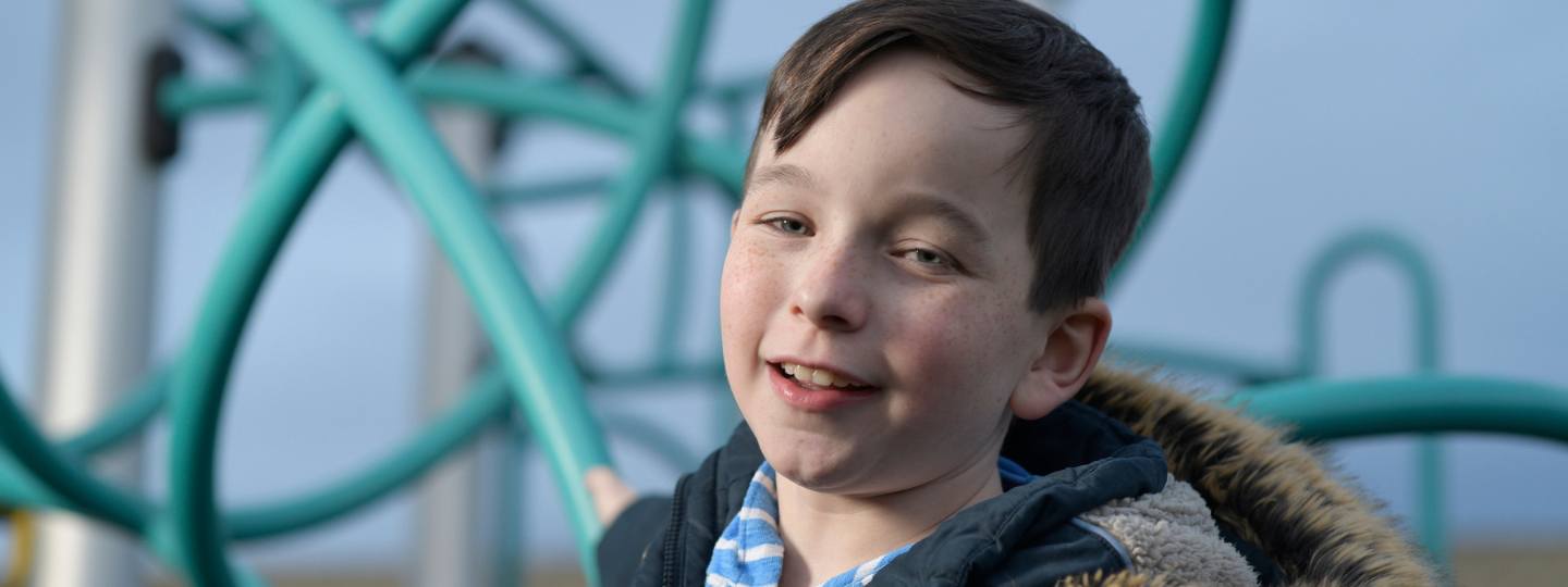 Smiling photo of William, who lives with juvenile idiopathic arthritis, on climbing frame outside