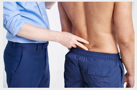 A doctor examining a mans back while he's stood straight.
