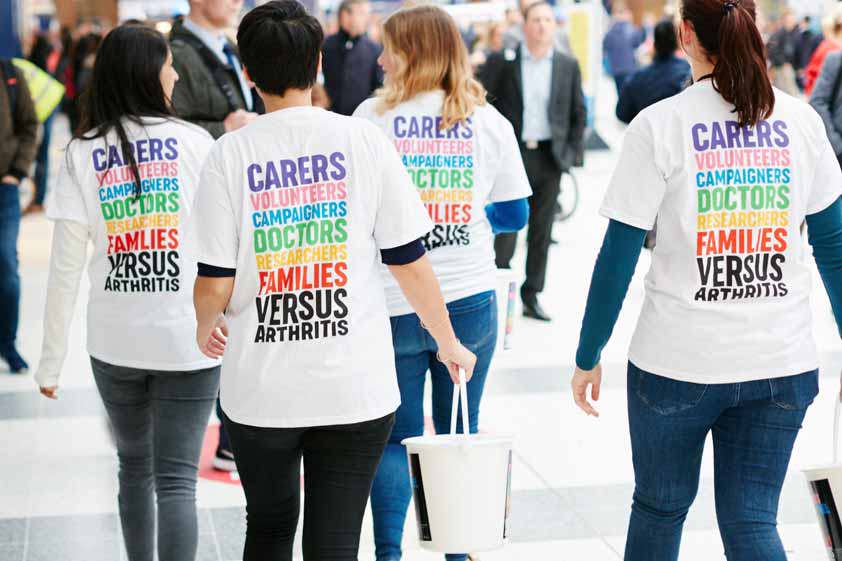 Versus Arthritis staff walking away from the camera with collection buckets.