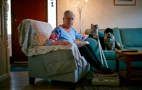 Brenda sitting in sofa beside her dog and crutches