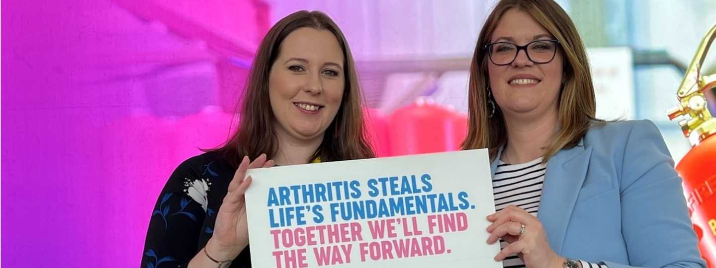 Two woman carrying a Versus Arthritis sign 
