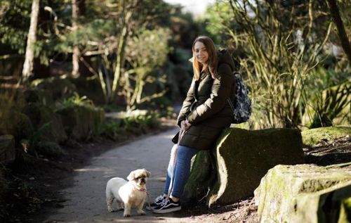 Young woman sitting on a stone wall beside her small white dog