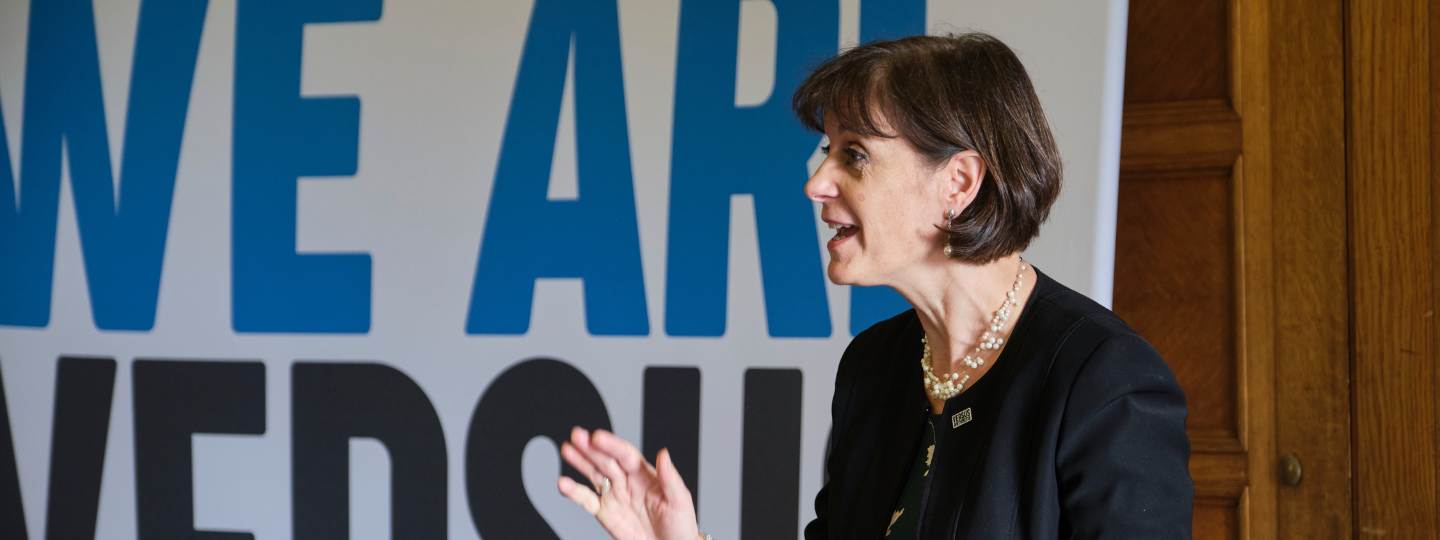 Deborah Alsina, CEO of Versus Arthritis, speaking at Stormont in front of Versus Arthritis sign