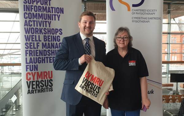 Elaine standing beside Samuel Kurtz MS who is holding a Versus Arthritis tote bag