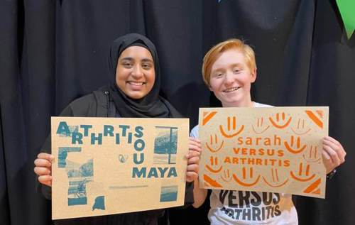 Smiling Sarah and Soumaya holding arthritis-related artwork