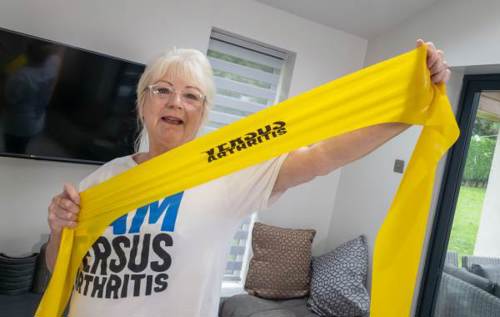 Janet wearing a Versus Arthritis t-shirt holding a yellow resistance band