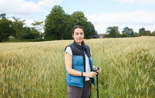 Phillipa wearing a vest and holding a walking stick in a field of wheat