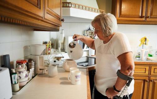 Christine, who lives with osteoarthritis, using a crutch and pouring a cup of tea