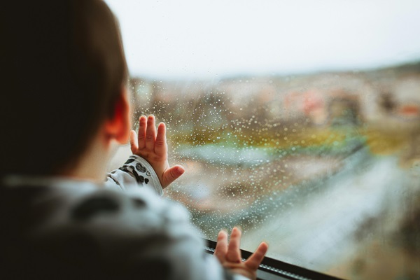 Young person with JIA looing out of a rainy window