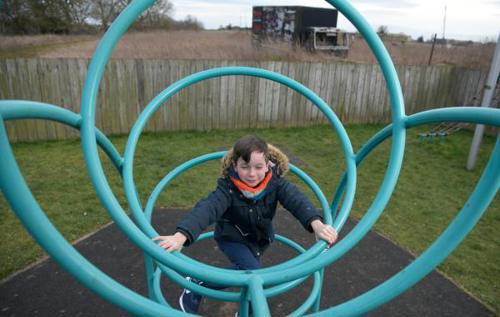 William, who lives with juvenile idiopathic arthritis, climbing a blue climbing frame in a playground