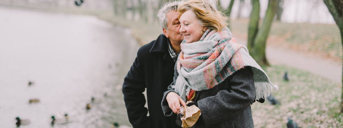 Woman and man wrapped up in warm coat and scarves feeding ducks