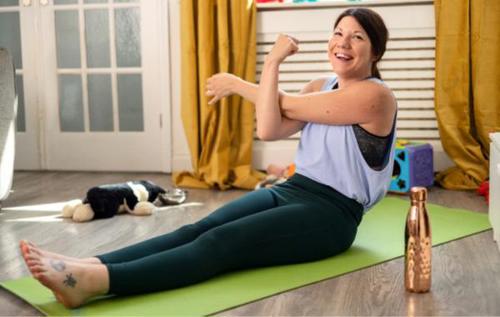 Smiling Jade wearing yoga clothes sitting on a green yoga mat stretching her arms