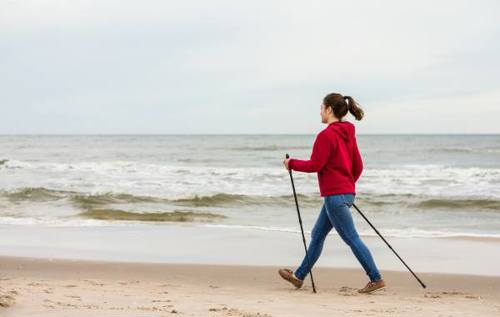 Woman wearing red jumper Nordic Walking along coastline